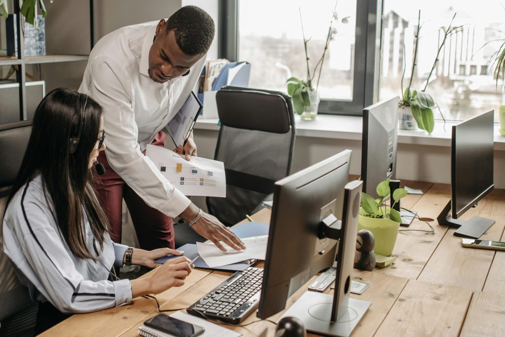 Two professionals discussing work at a computer in a bright, modern office space.